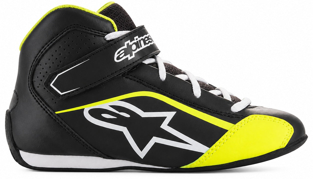 Alpinestars high-top racing shoe in black with neon yellow and white accents, featuring a white Alpinestars star logo on the side and a white Alpinestars brand strap across the ankle.