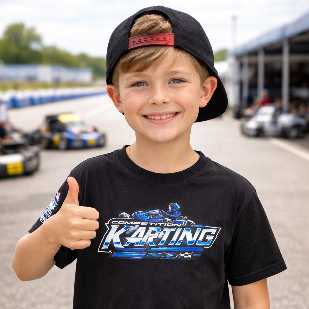 Kid wearing Competition Karting t-shirt giving thumbs up at a kart racing track paddock with go karts in the background