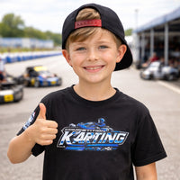 Thumbnail for Kid wearing Competition Karting t-shirt giving thumbs up at a kart racing track paddock with go karts in the background